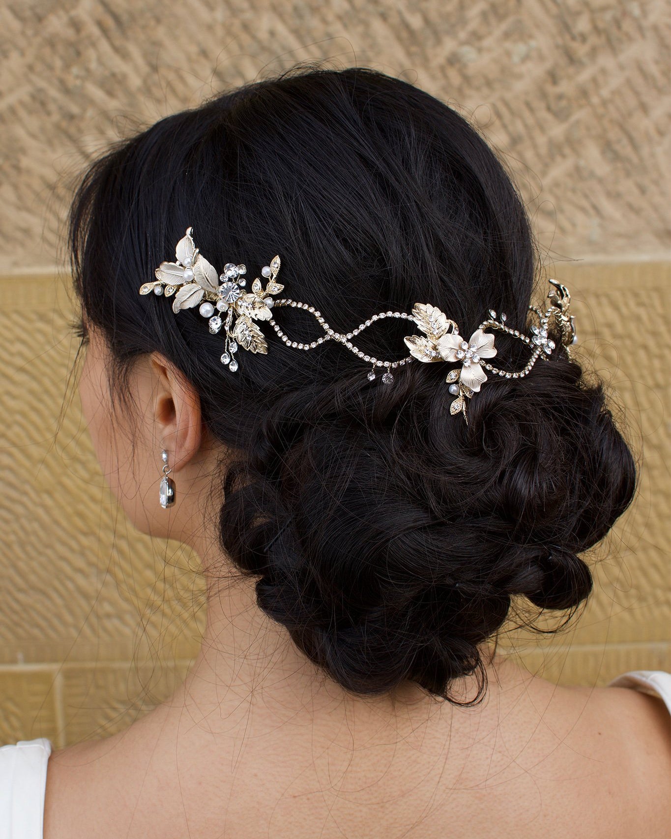 A dark haired model with curly hair wears a pale gold vine at the back of her head