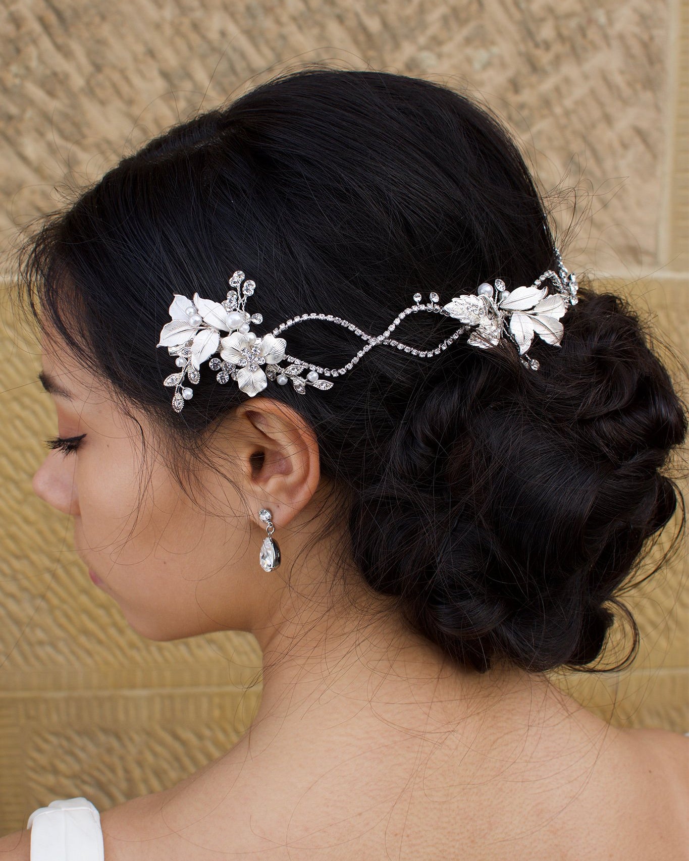 A dark haired model with curly hair wears a silver vine at the back of her head with stone background