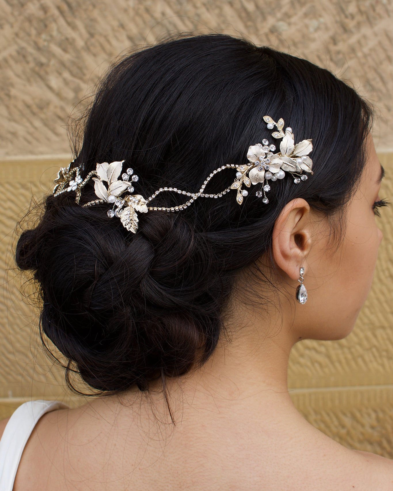 A dark haired model with curly hair wears a Gold vine at the back of her head with a stone background