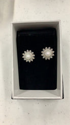 A pair of silver-toned flower-shaped stud earrings with white pearl centers and clear stones, presented in a white jewelry box with a black velvet insert.