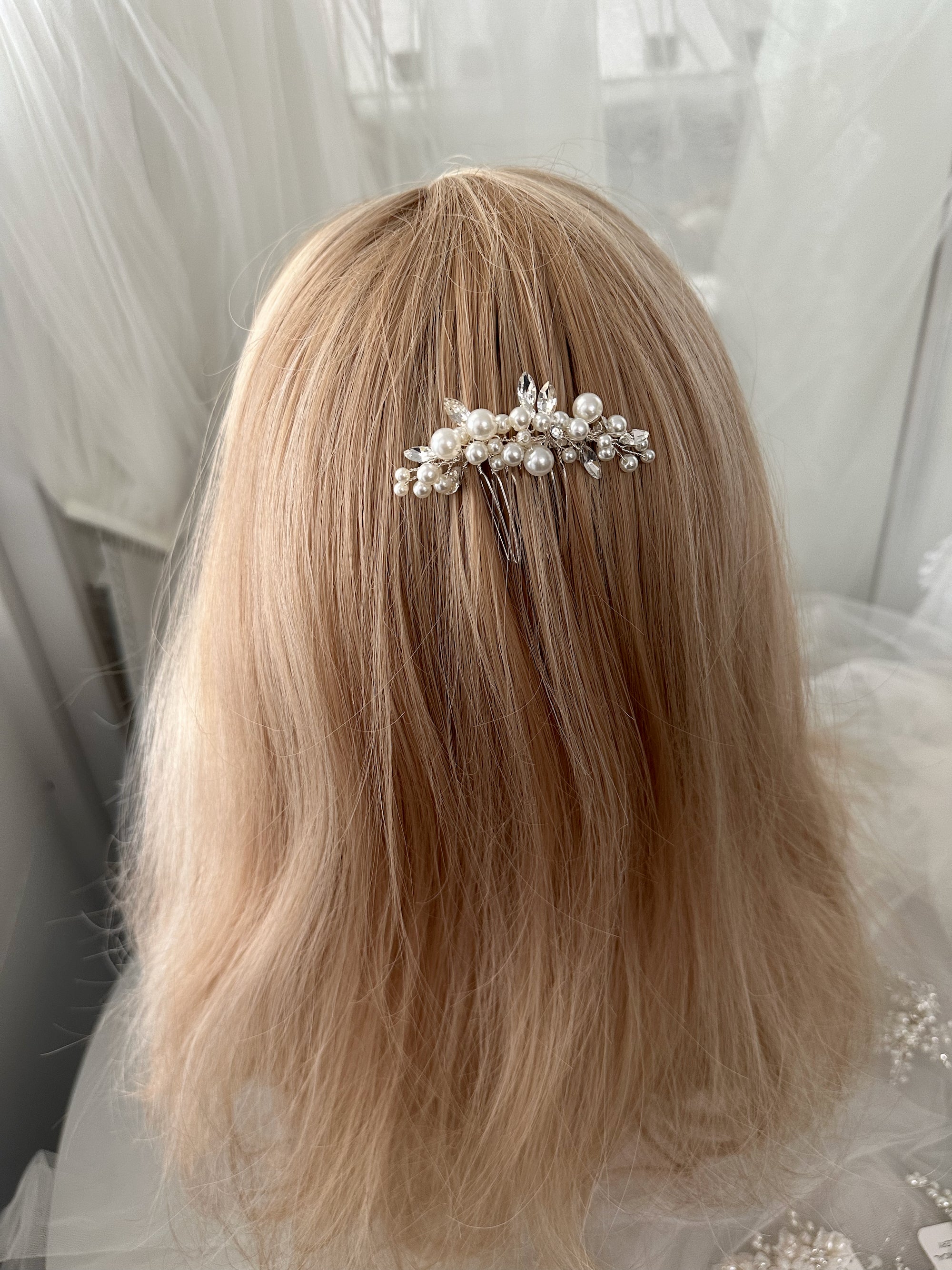 Hair accessory with pearls on a person with blonde hair, wearing a sheer white garment.