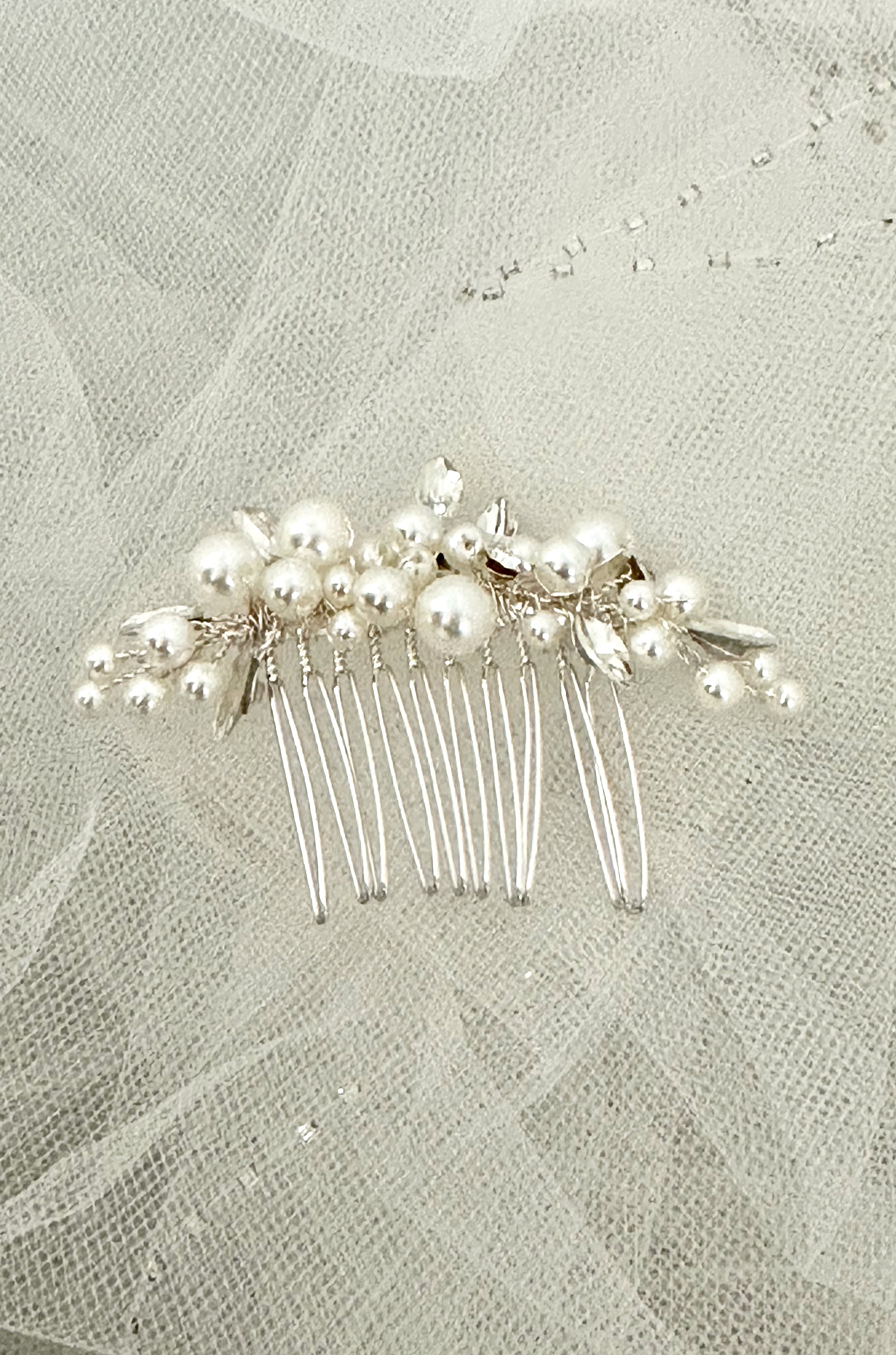 Silver hair comb with pearls on a textured fabric background