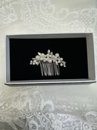 Silver hair comb with pearls on a black card inside a box, placed on lace fabric.