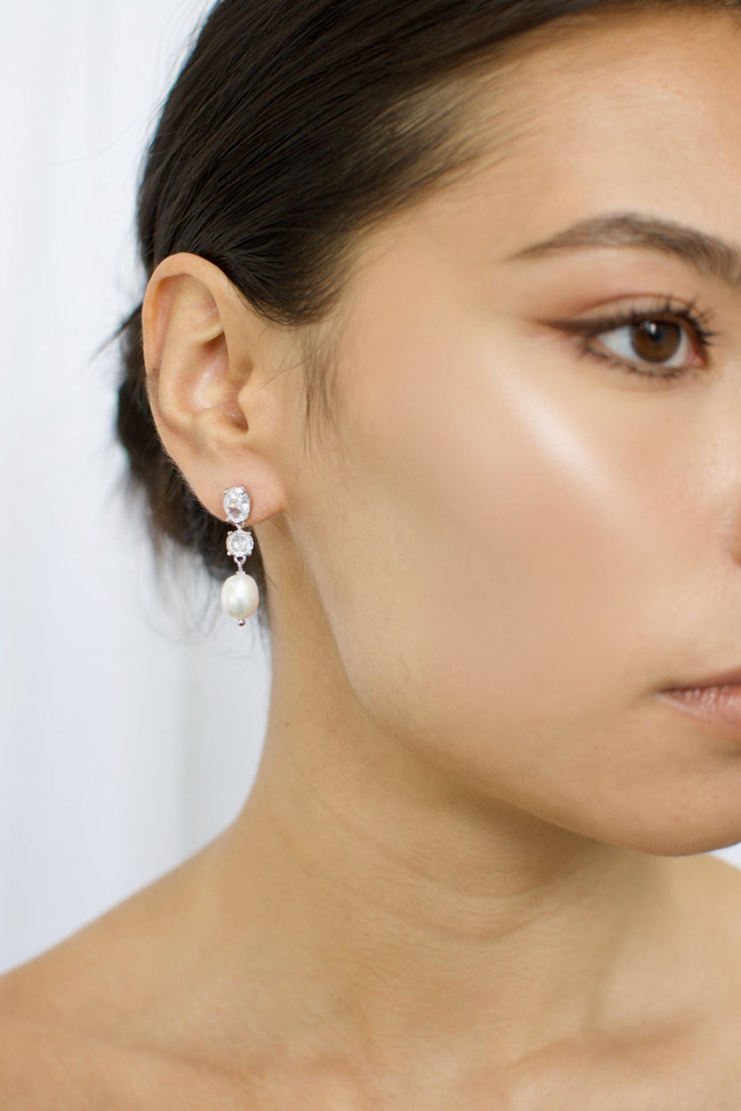 Close-up of a woman wearing pearl earrings with a plain background
