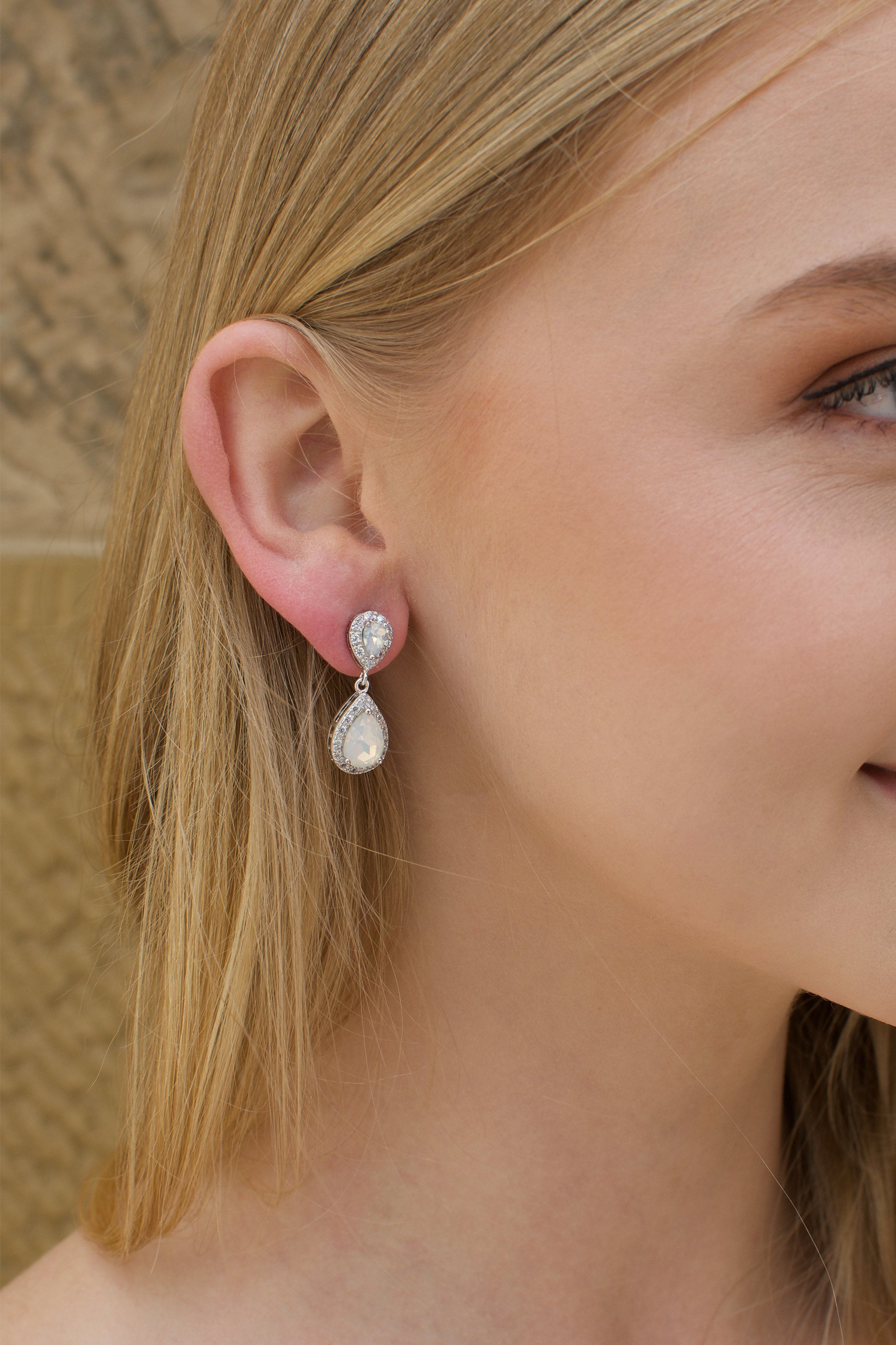 A blonde model bride wears a double teardrop earring with white opal colour stones 