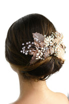 A model with brown hair wears a rose gold and filigree leaves Bridal Vine at the back of her head against a white background