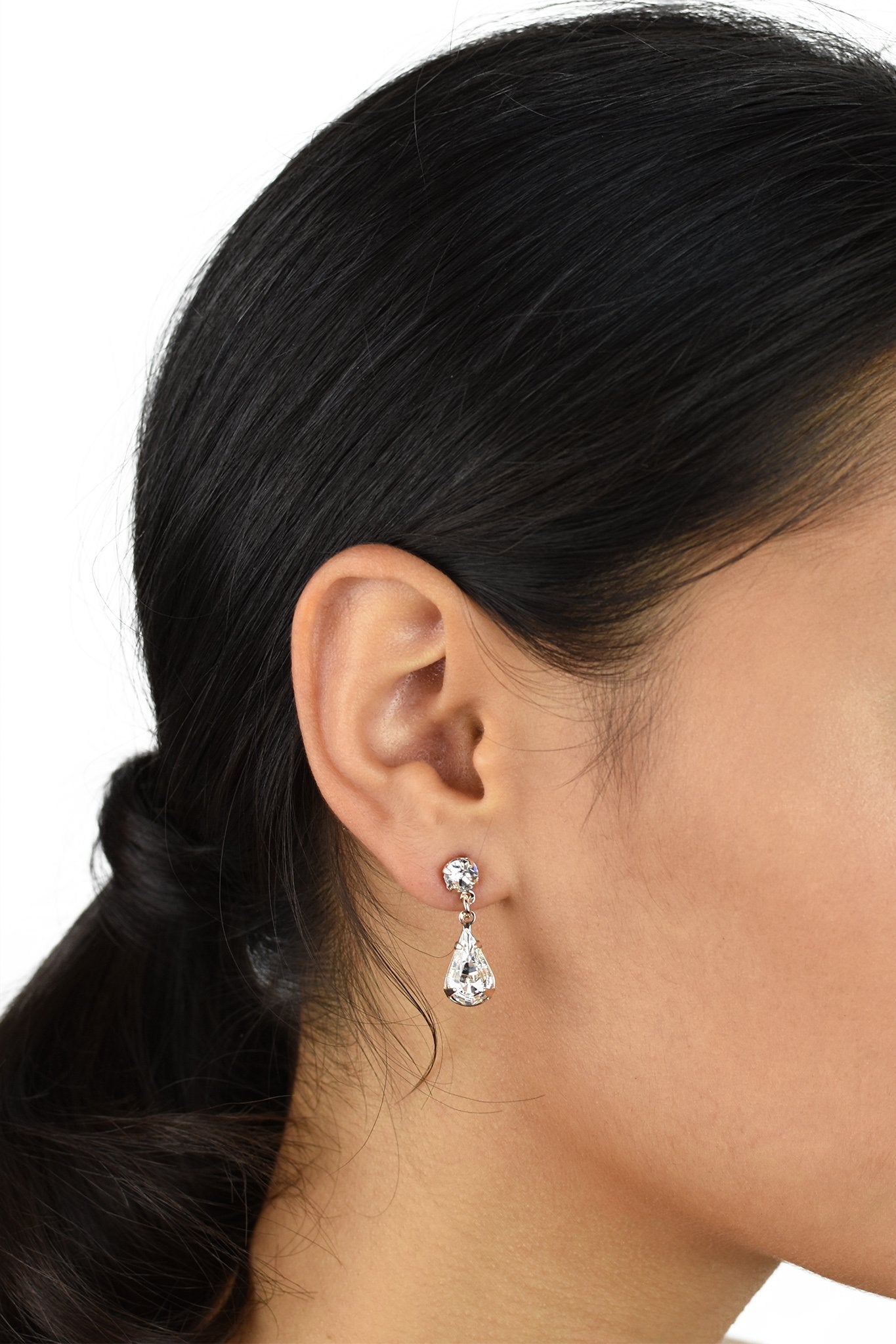 A model with black hair wears a rose gold teardrop earring in her ear against a white background