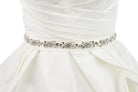 A belt of teardrop shape crystals is around the waist of an ivory satin wedding gown with a white background. 