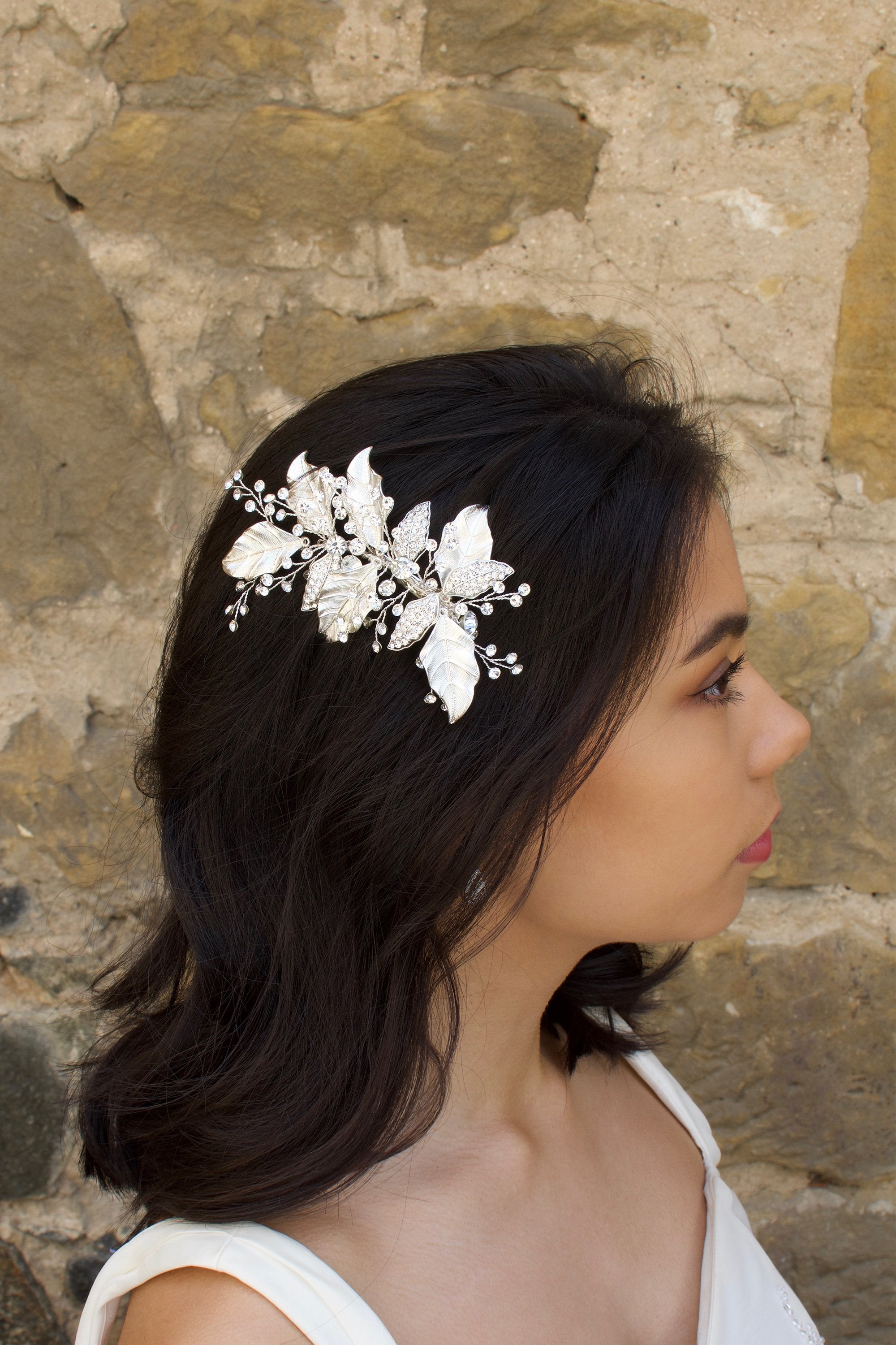 Silver Leaves Side Comb with sprigs of stones worn by a dark hair model with a stone wall backdrop