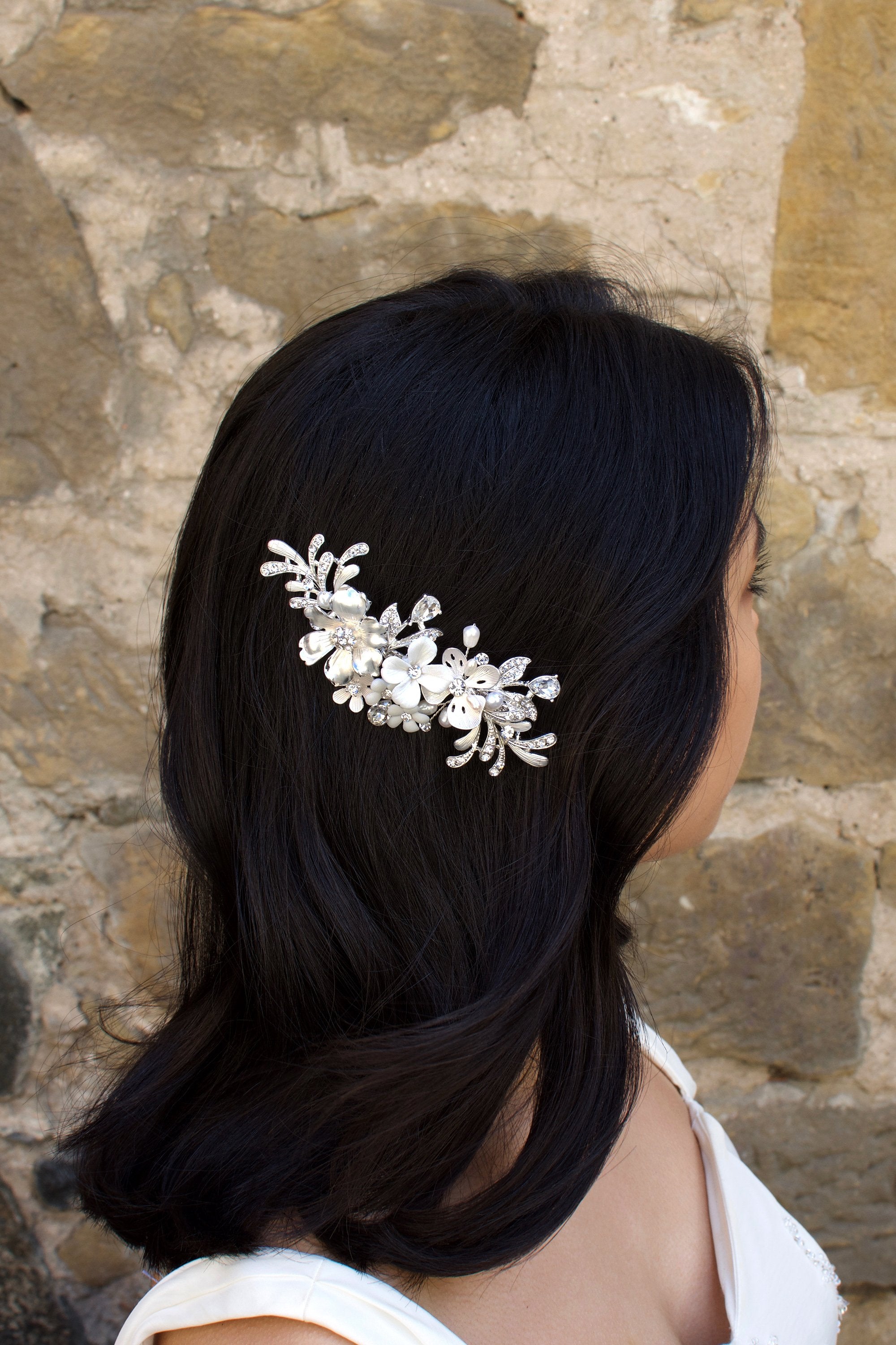 Model with dark hair wears a silver and flower side comb with a stone wall backdrop