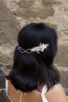 A Black haired model with her hair down wears a soft bridal vine at the back of her head. Stone wall background